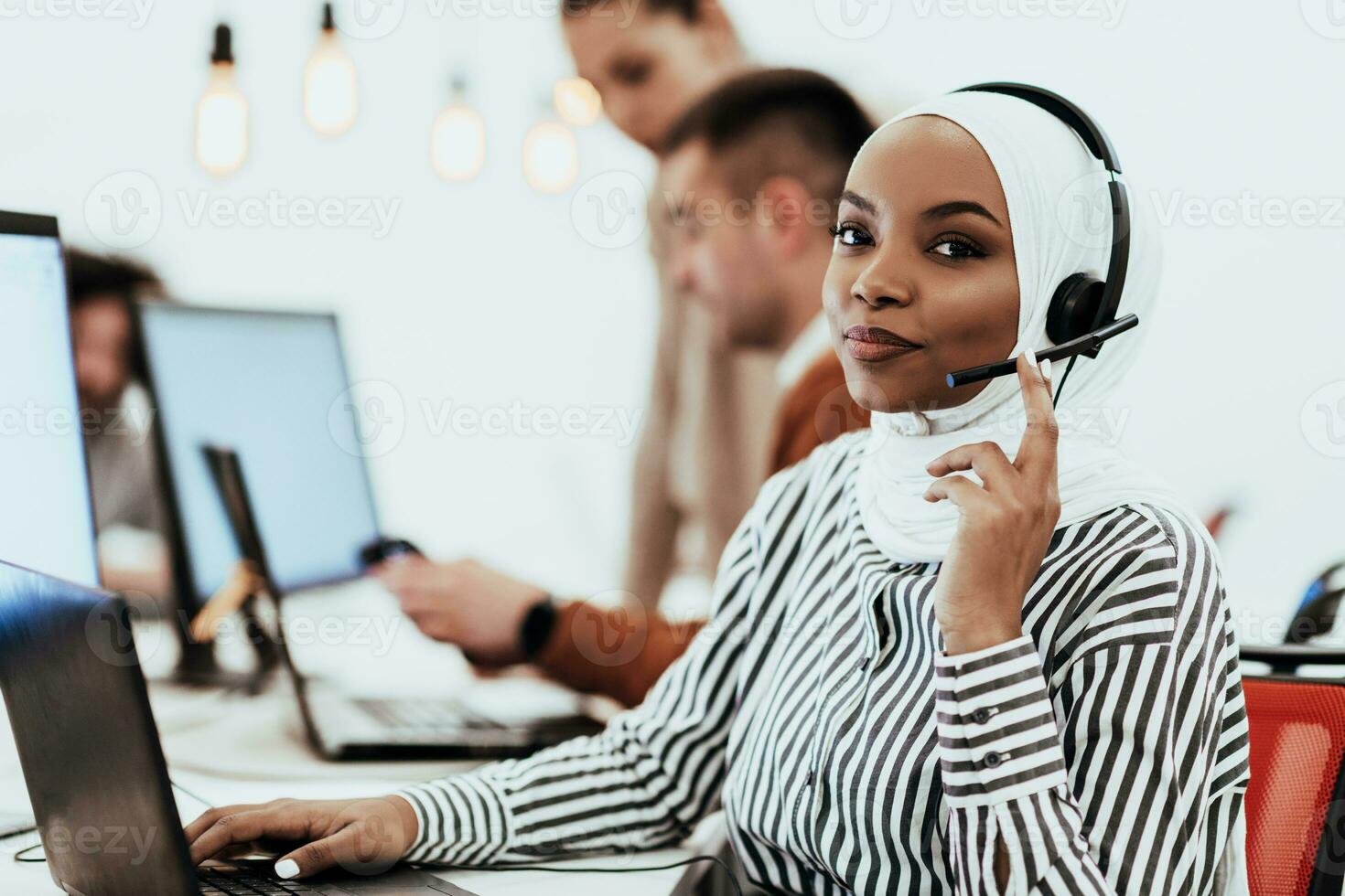 African American muslim woman with hijab and headset working as customer support in a modern office. photo