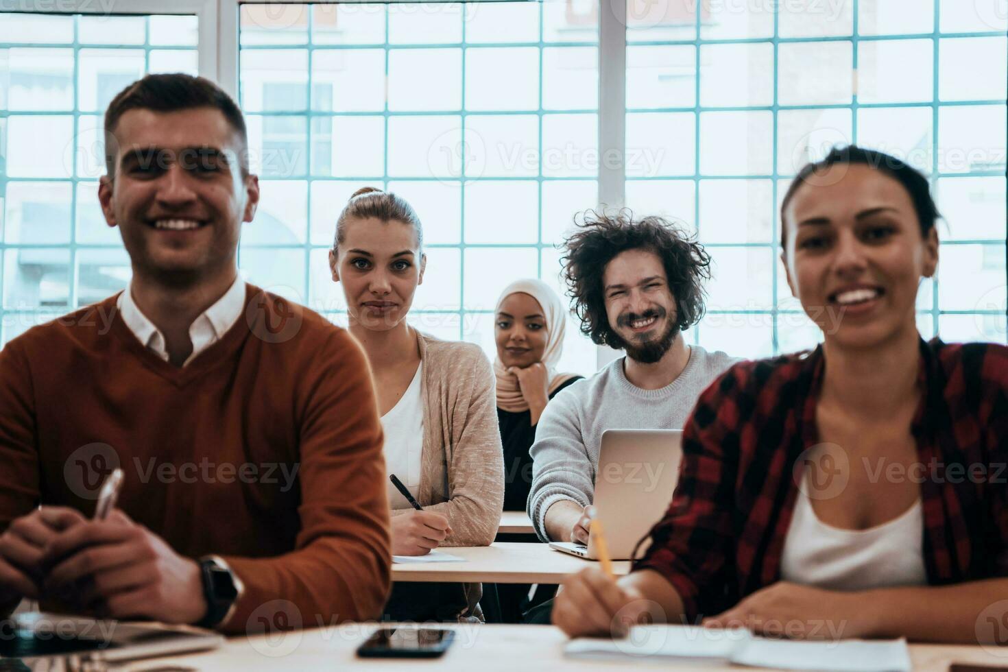 A group of diverse young men and women sit in a modern classroom and listen to a lecture on business training photo