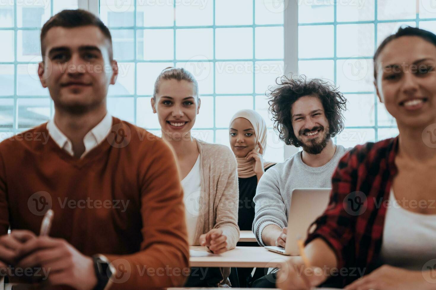 A group of diverse young men and women sit in a modern classroom and listen to a lecture on business training photo
