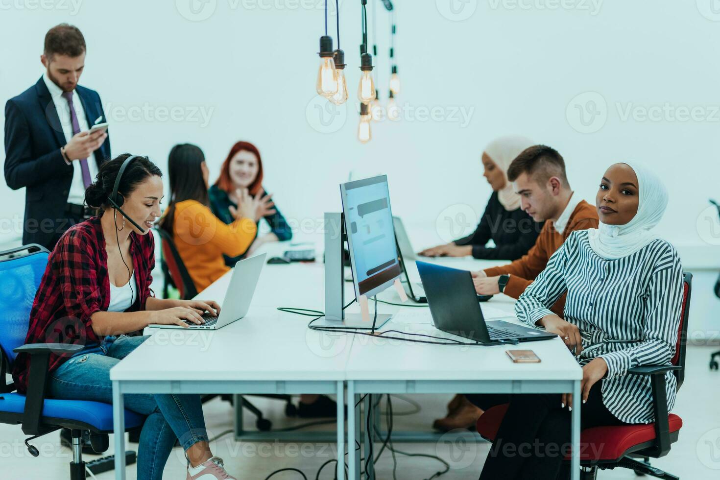 grupo de multiétnico colegas trabajando en escritorio ordenadores, ordenador portátil y compartiendo su ideas en un moderno oficina espacio.joven influencers trabajo en en línea márketing proyectos foto