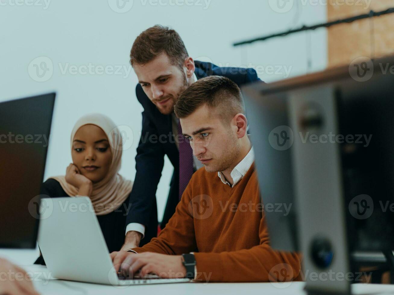 Group of multi-ethnic colleagues working on desktop computers, laptop and sharing their ideas in a modern office space.Young influencers work on online marketing projects. photo