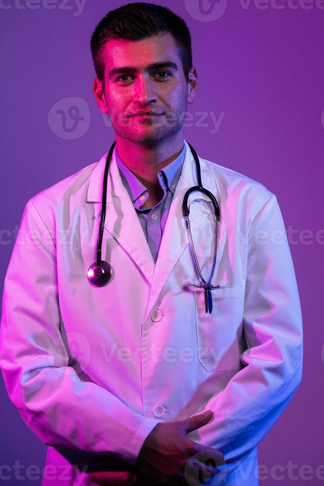 coronavirus covid-19 peligro alerta retrato de héroe en blanco abrigo. alegre sonriente joven médico con estetoscopio en médico hospital en pie en contra azul y rosado antecedentes. foto