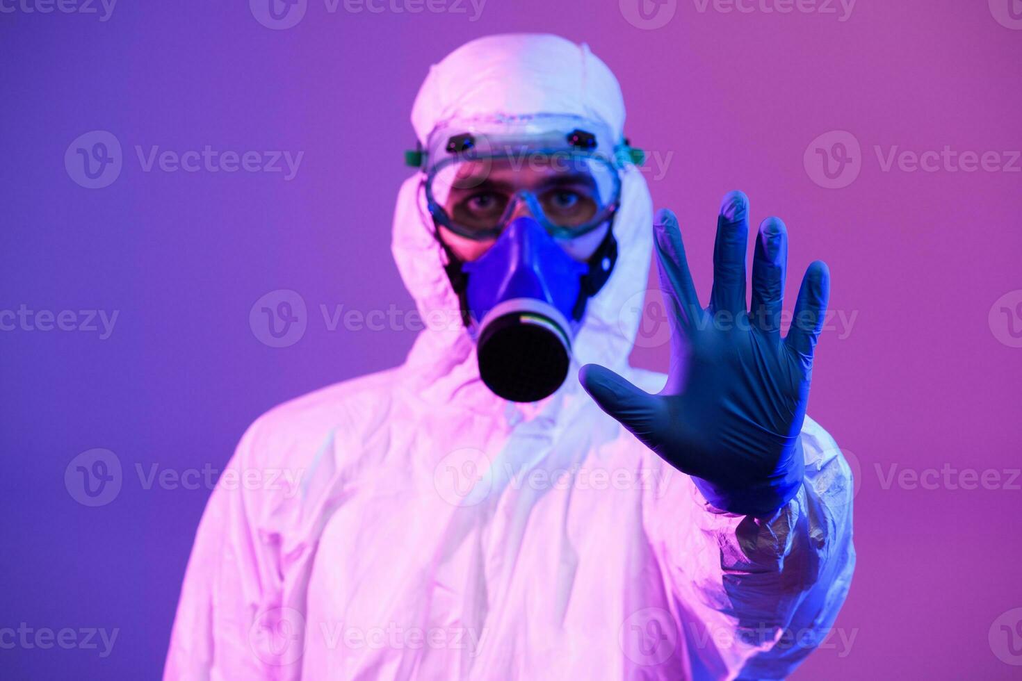 Coronavirus covid-19 pandemic. Doctor scientist wearing protective biological suit and mask due to global healthcare epidemic warning and danger background in blue and pink neon lights background. photo