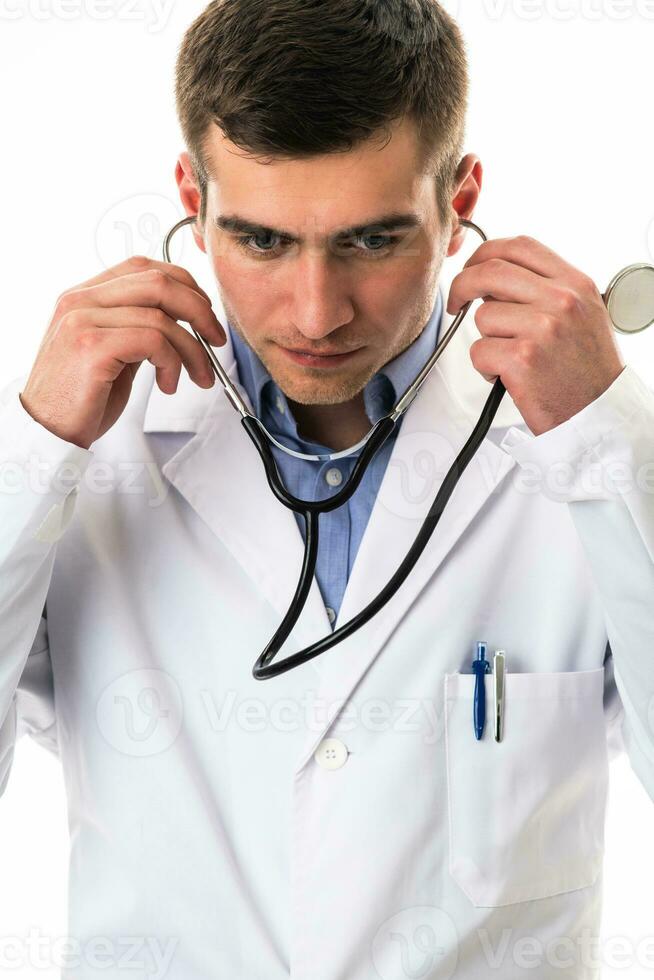 Portrait of hero in a white coat. Cheerful smiling young doctor with a stethoscope in a medical hospital standing against a white background. Coronavirus covid-19 danger alert photo