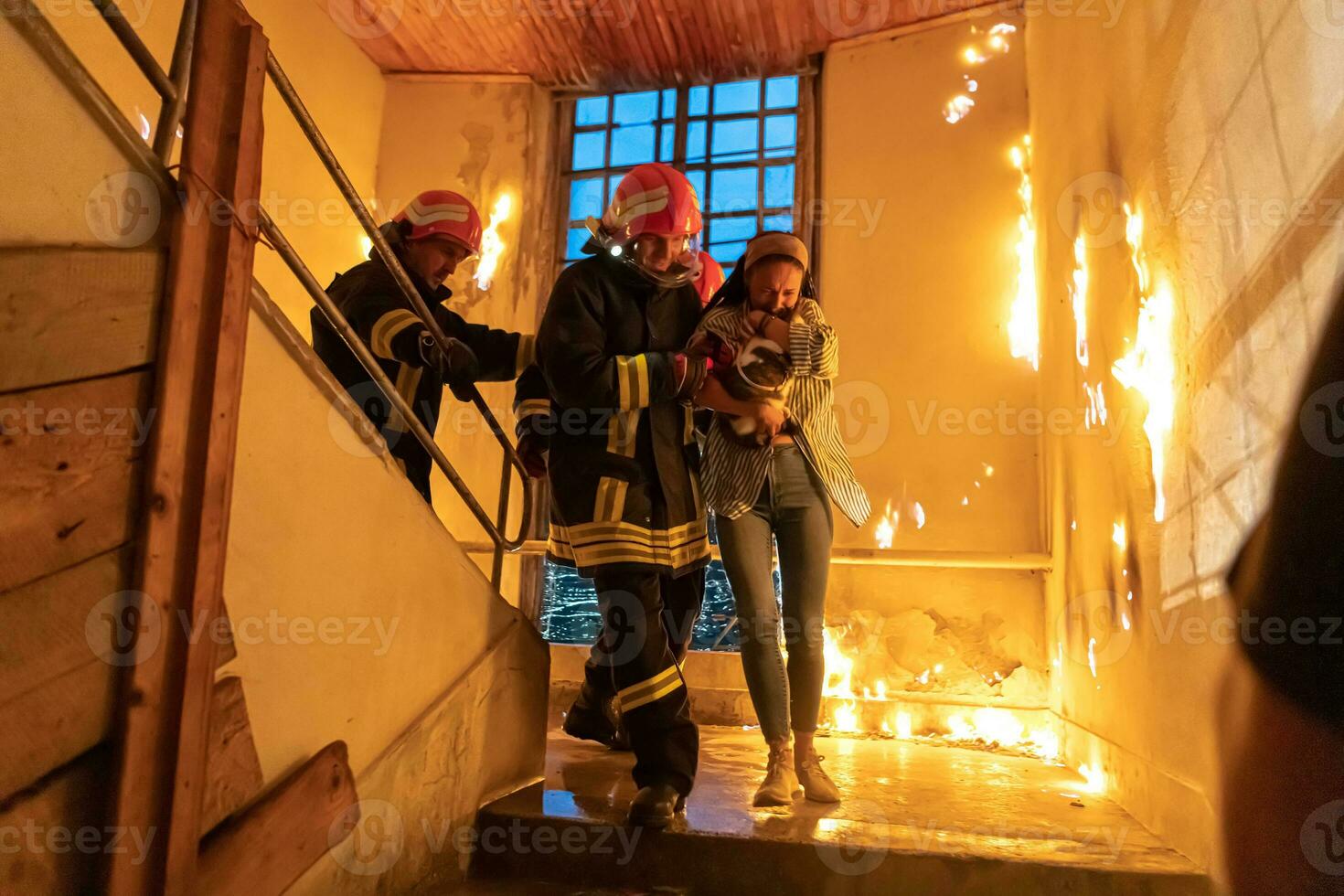 Brave Fireman Descends Stairs of a Burning Building and Holds Saved Girl in His Arms. Open fire and one Firefighter in the Background. photo