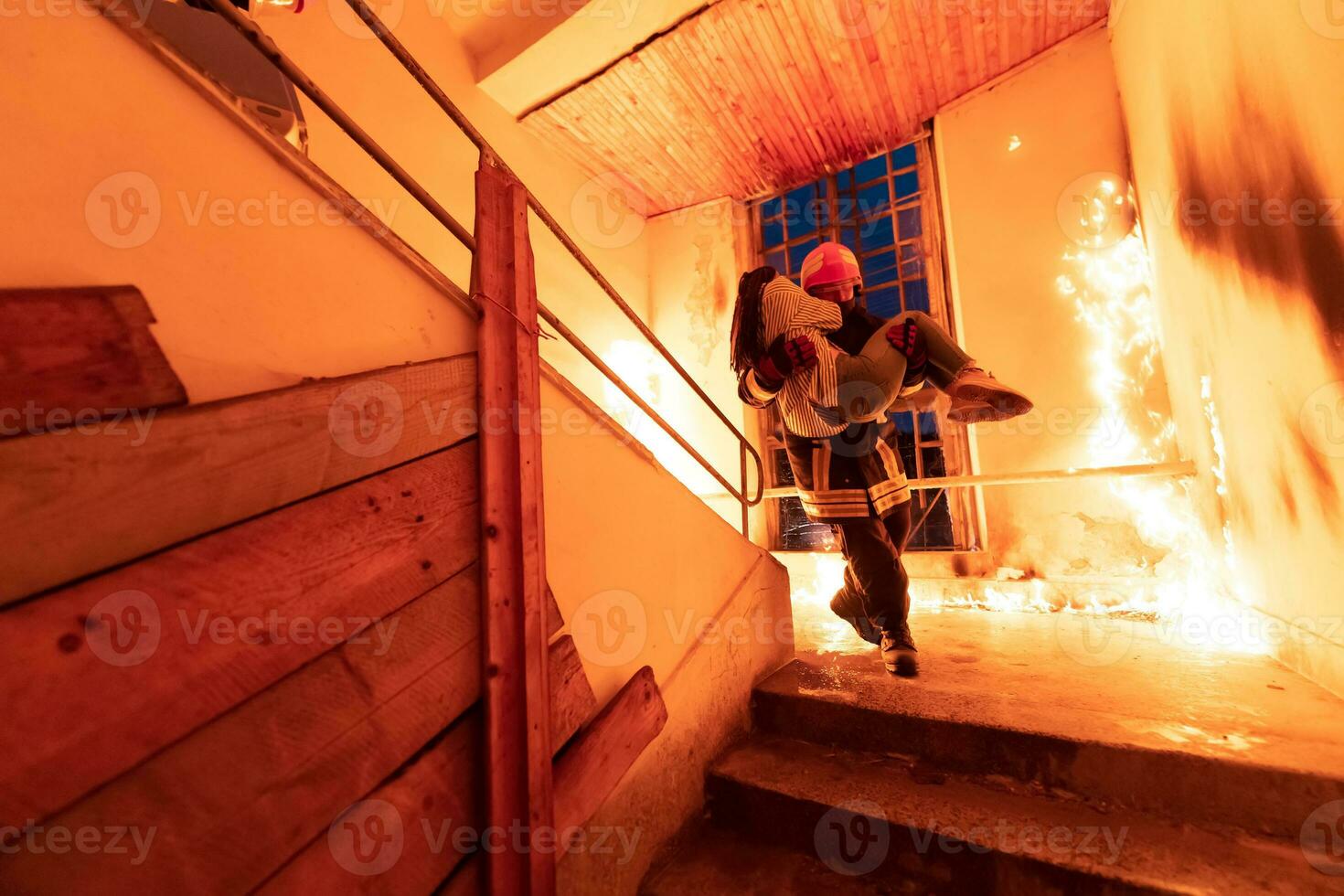 Brave Fireman Descends Stairs of a Burning Building and Holds Saved Girl in His Arms. Open fire and one Firefighter in the Background. photo