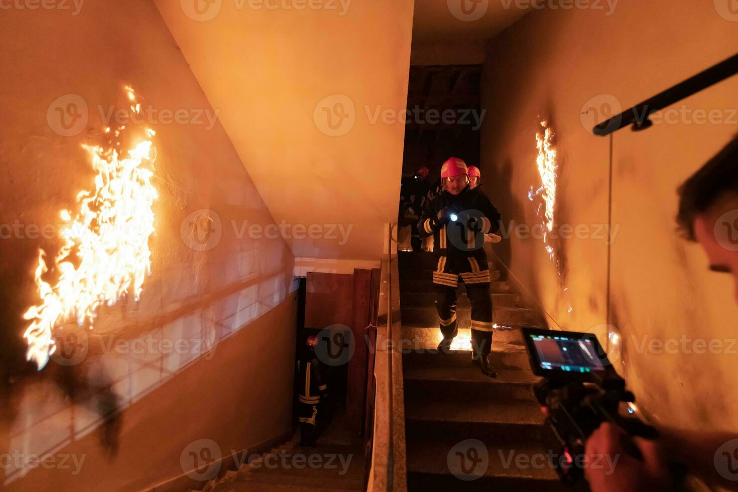 Brave Fireman Descends Stairs of a Burning Building and Holds Saved Girl in His Arms. Open fire and one Firefighter in the Background. photo