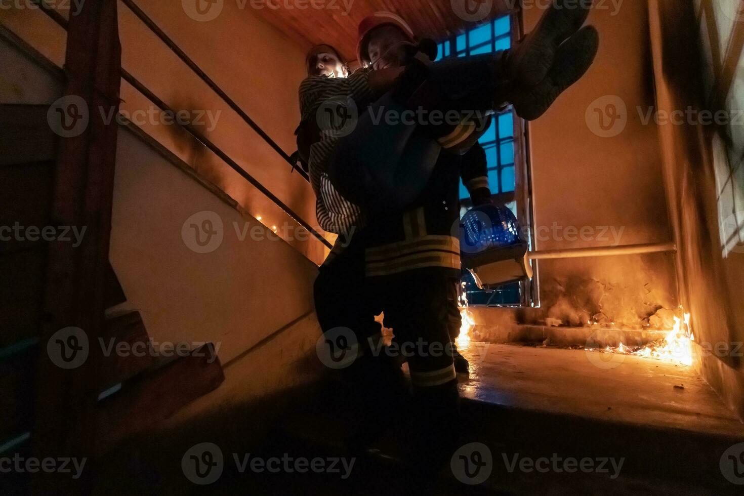 valiente bombero desciende escalera de un ardiente edificio y sostiene salvado niña en su brazos. abierto fuego y uno bombero en el antecedentes. foto