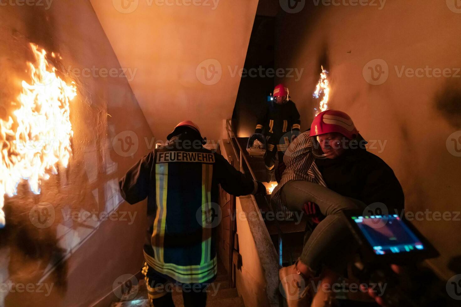 Brave Fireman Descends Stairs of a Burning Building and Holds Saved Girl in His Arms. Open fire and one Firefighter in the Background. photo