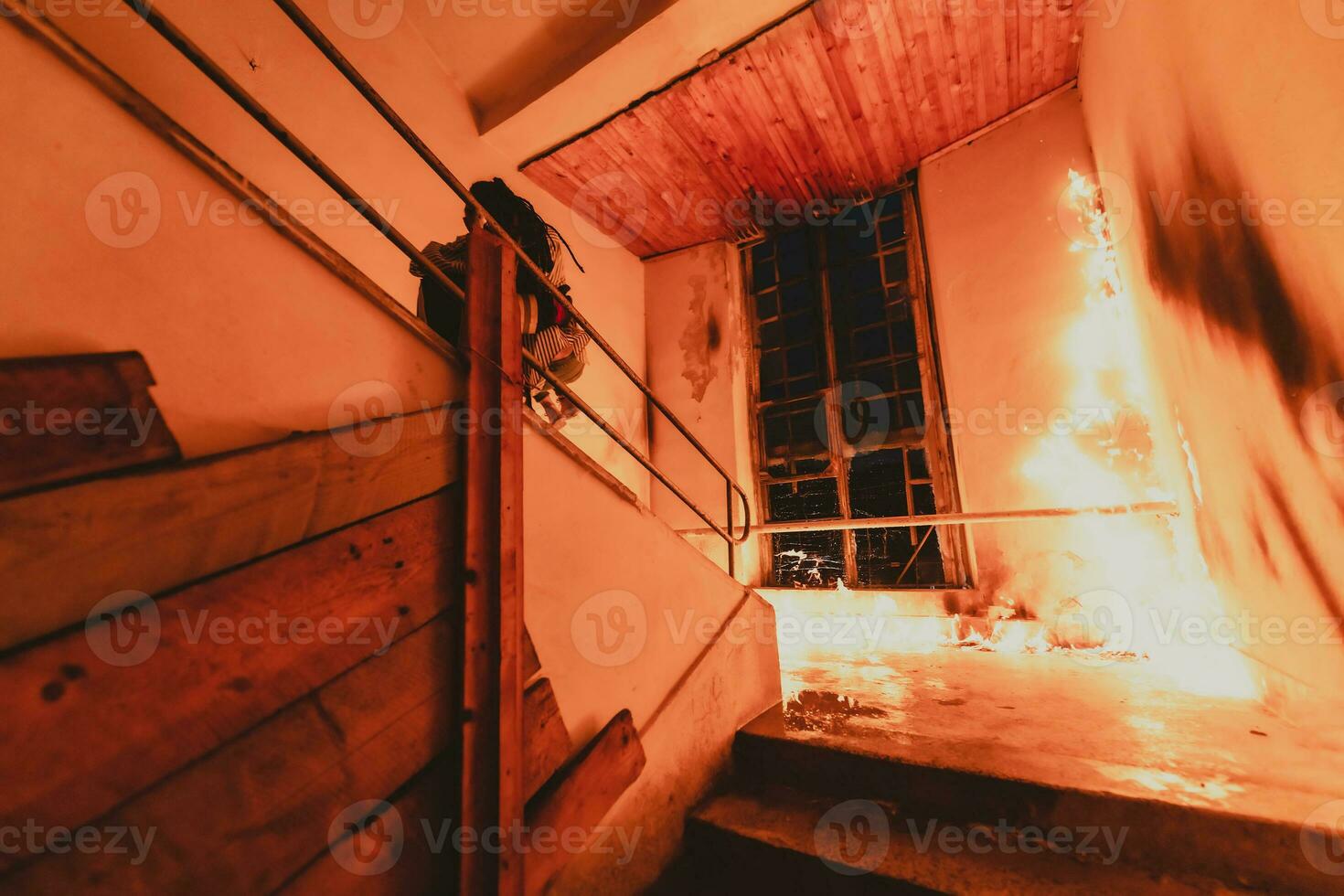 Brave Fireman Descends Stairs of a Burning Building and Holds Saved Girl in His Arms. Open fire and one Firefighter in the Background. photo