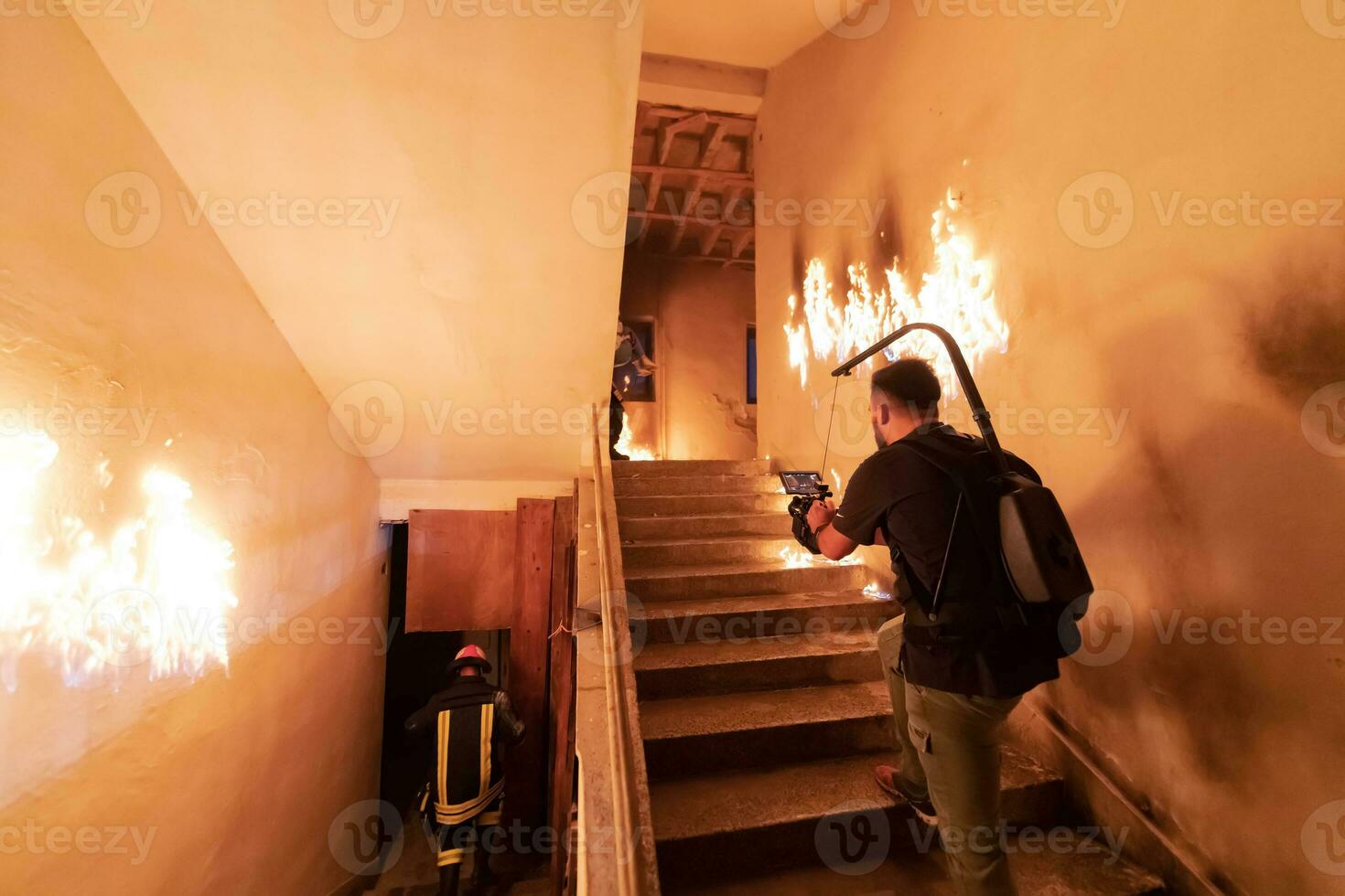 Brave Fireman Descends Stairs of a Burning Building and Holds Saved Girl in His Arms. Open fire. Cinematographer taking shoot with pro cinema camera and three-axis gimbal stabilization. low light photo
