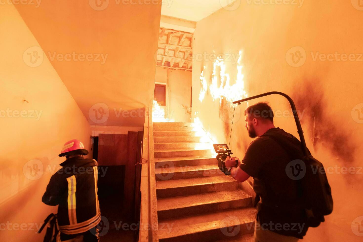 Brave Fireman Descends Stairs of a Burning Building and Holds Saved Girl in His Arms. Open fire. Cinematographer taking shoot with pro cinema camera and three-axis gimbal stabilization. low light photo