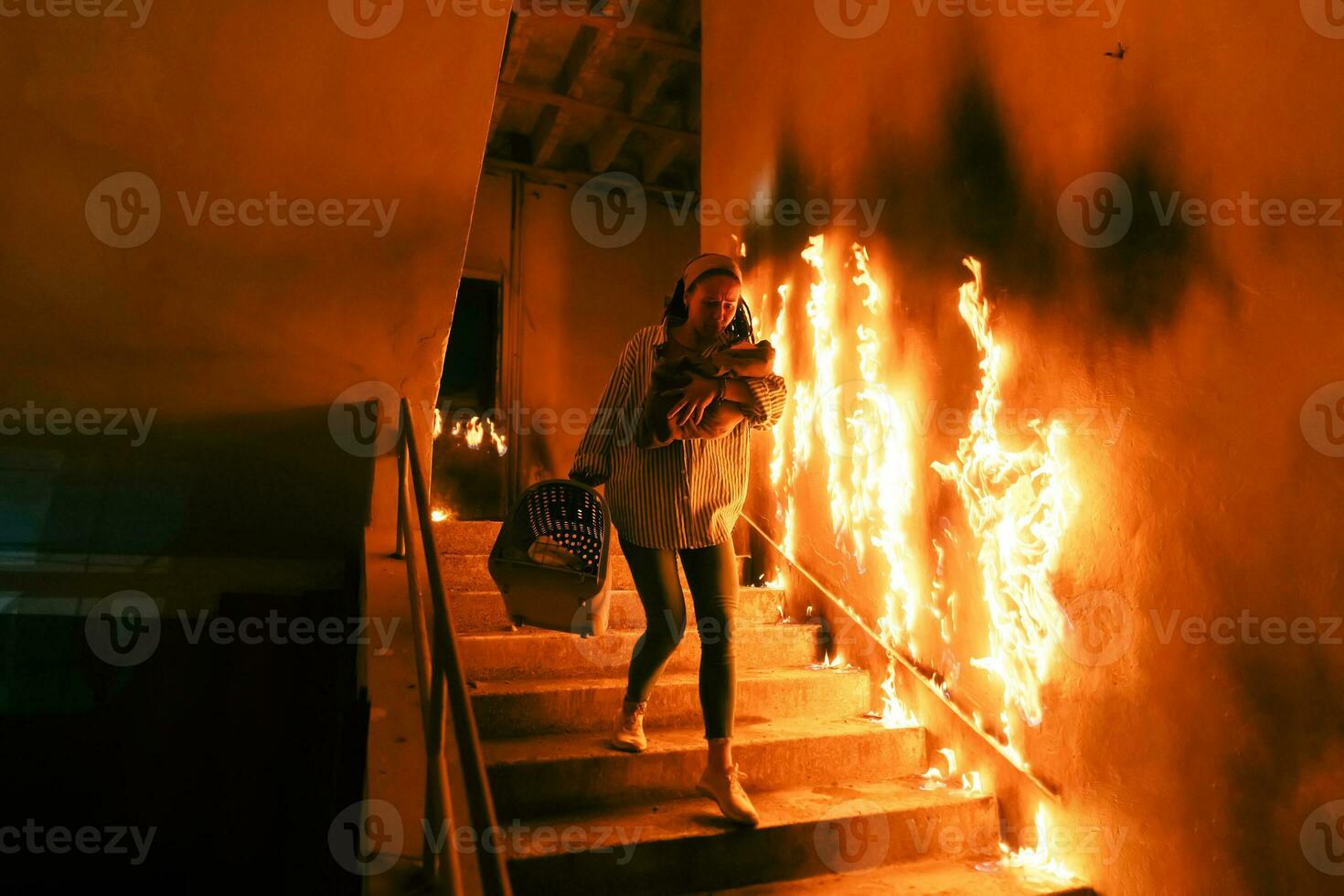 Brave Fireman Descends Stairs of a Burning Building and Holds Saved Girl in His Arms. Open fire and one Firefighter in the Background. photo