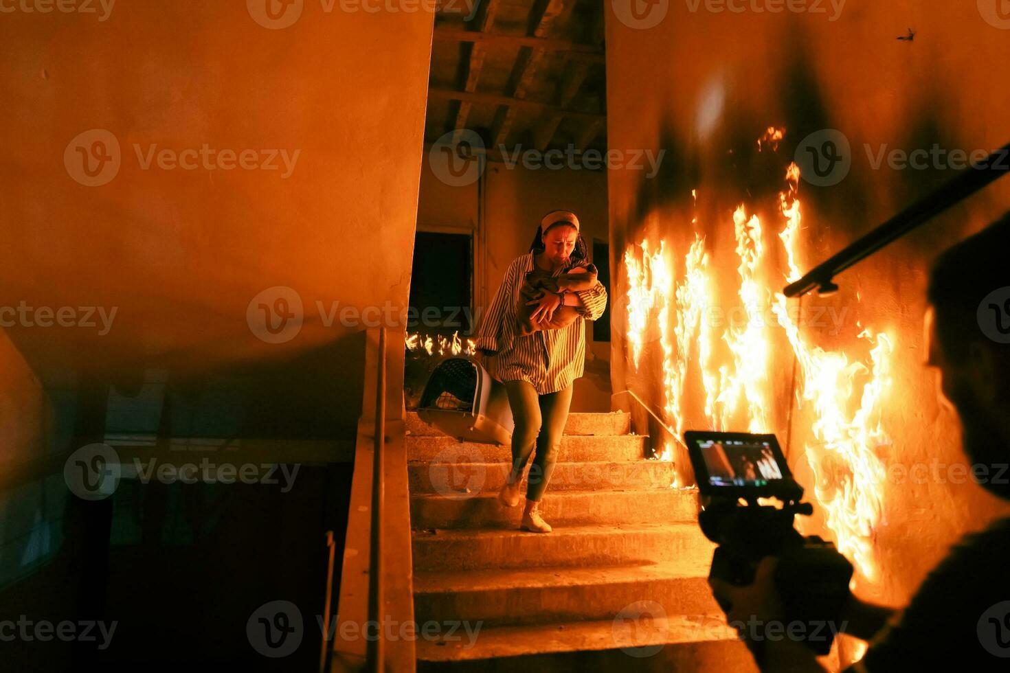 Brave Fireman Descends Stairs of a Burning Building and Holds Saved Girl in His Arms. Open fire and one Firefighter in the Background. photo