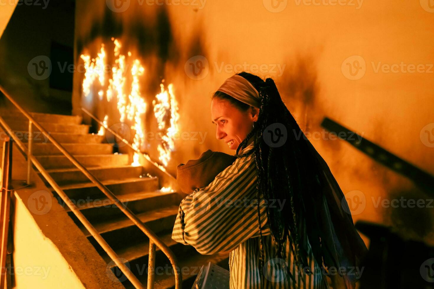 Brave Fireman Descends Stairs of a Burning Building and Holds Saved Girl in His Arms. Open fire and one Firefighter in the Background. photo