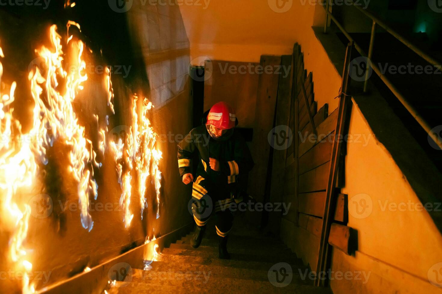 Brave Fireman Descends Stairs of a Burning Building and Holds Saved Girl in His Arms. Open fire and one Firefighter in the Background. photo