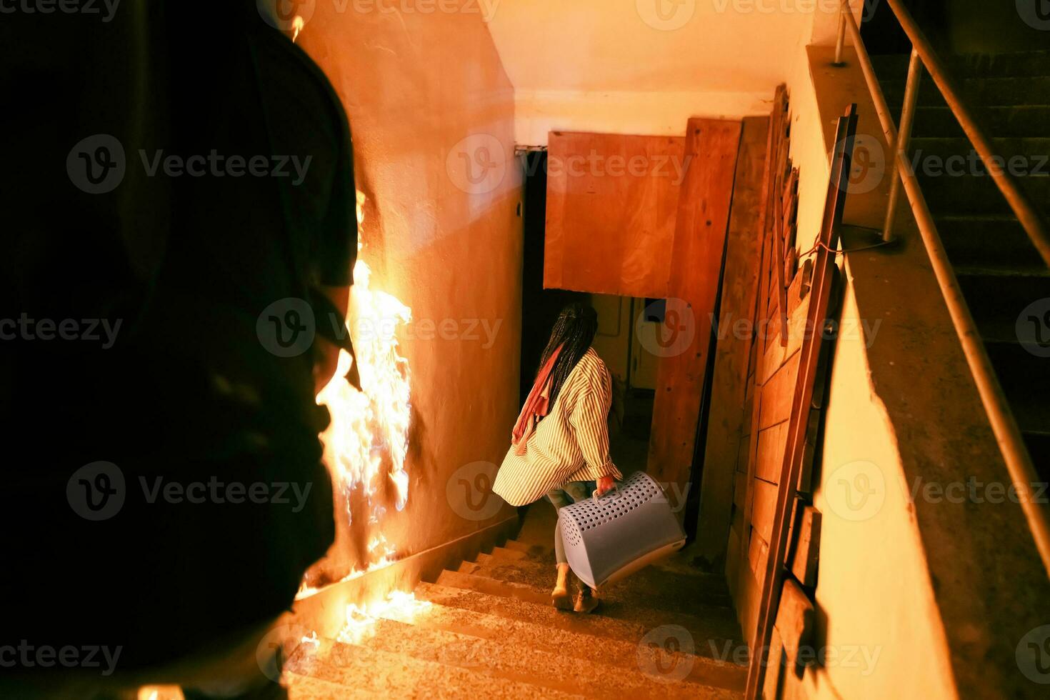 Brave Fireman Descends Stairs of a Burning Building and Holds Saved Girl in His Arms. Open fire and one Firefighter in the Background. photo