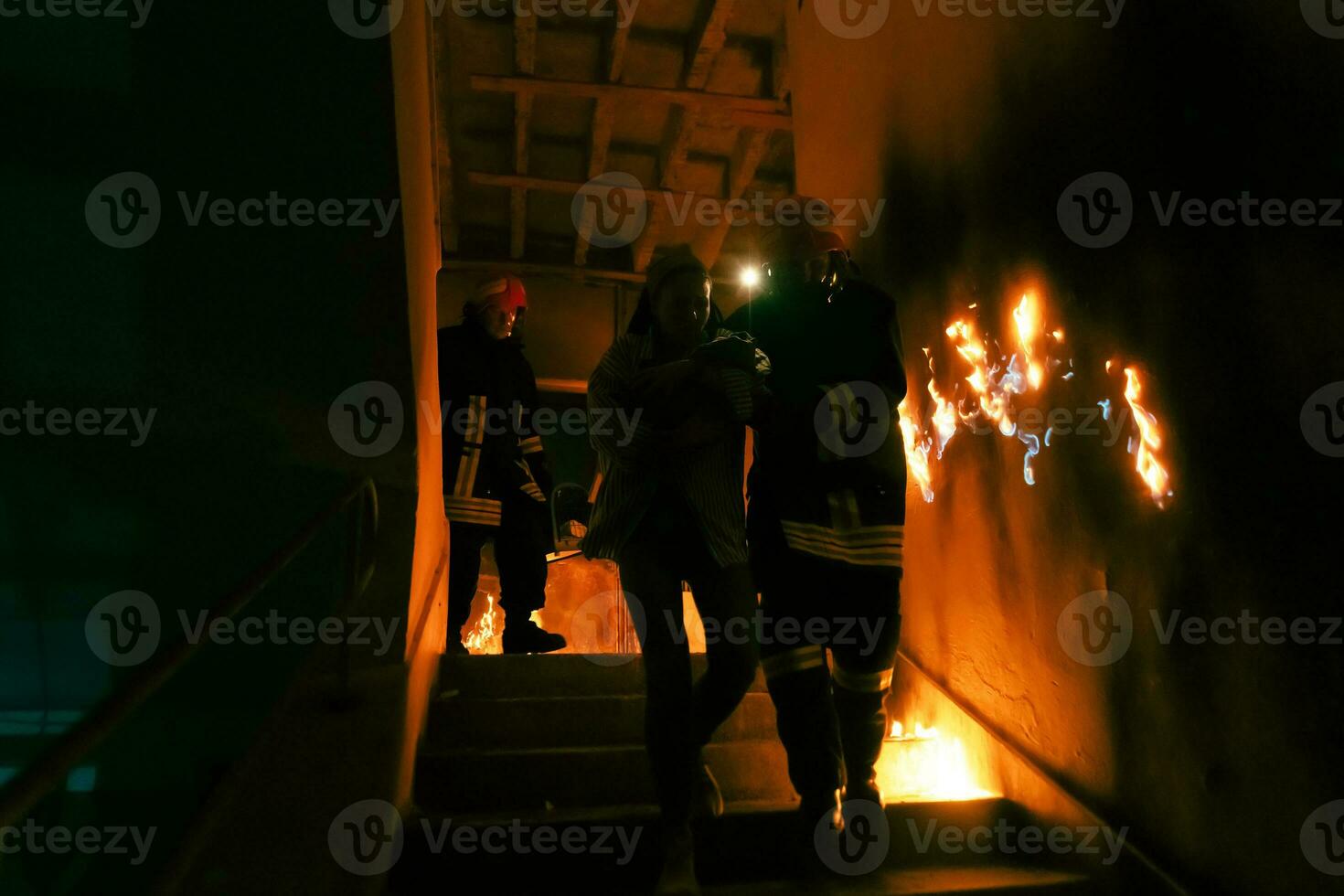 Brave Fireman Descends Stairs of a Burning Building and Holds Saved Girl in His Arms. Open fire and one Firefighter in the Background. photo