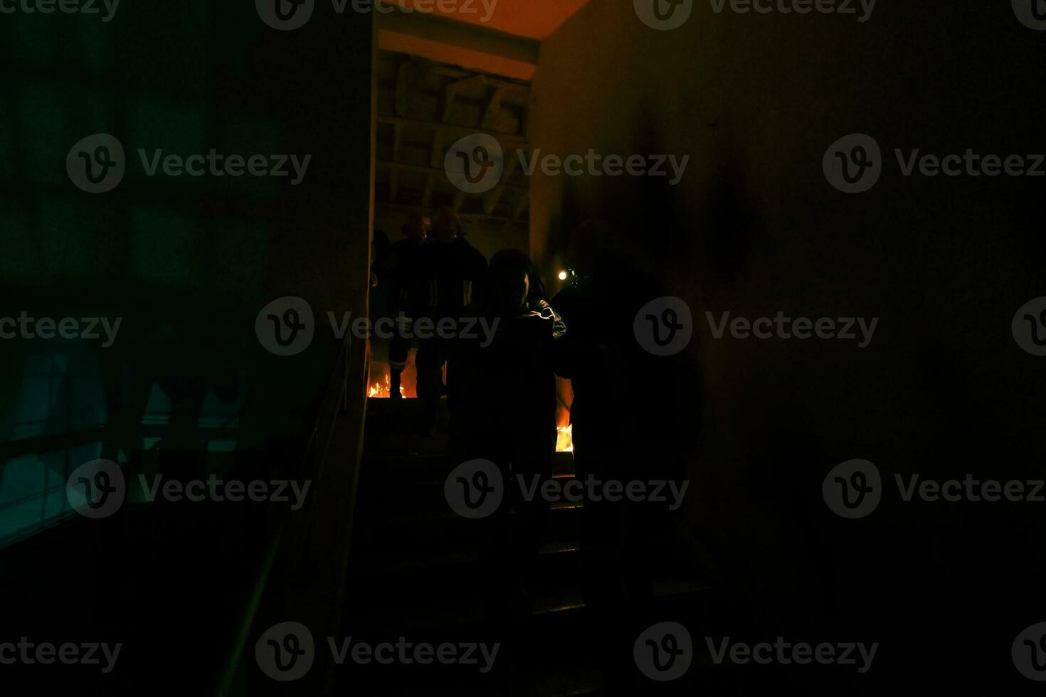 Brave Fireman Descends Stairs of a Burning Building and Holds Saved Girl in His Arms. Open fire and one Firefighter in the Background. photo