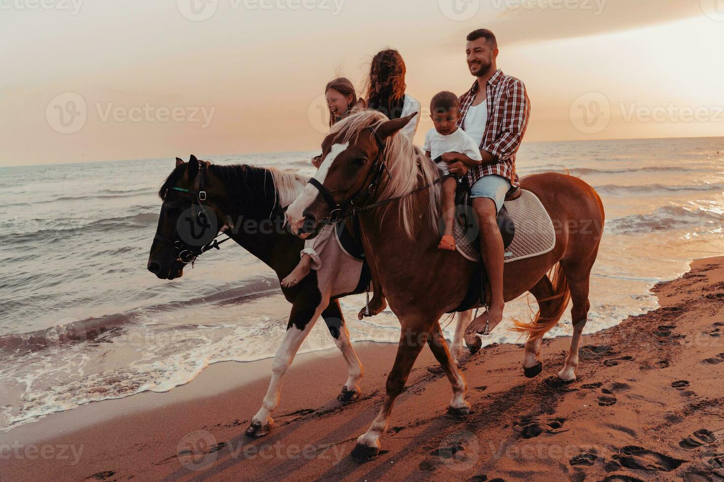 The family spends time with their children while riding horses together on a sandy beach. Selective focus photo