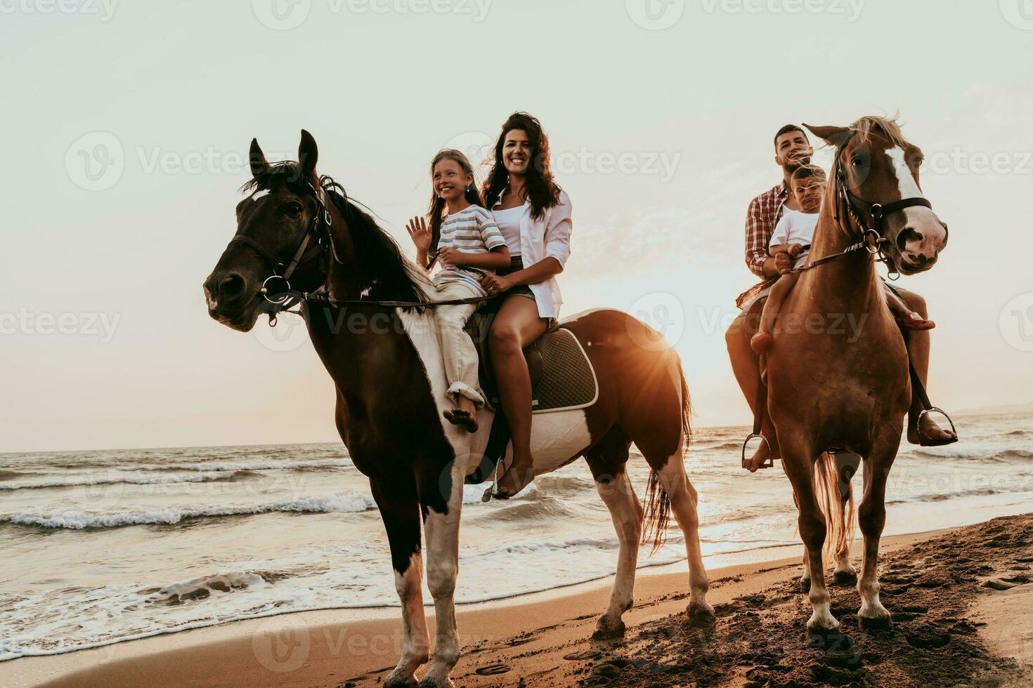 The family spends time with their children while riding horses together on a sandy beach. Selective focus photo