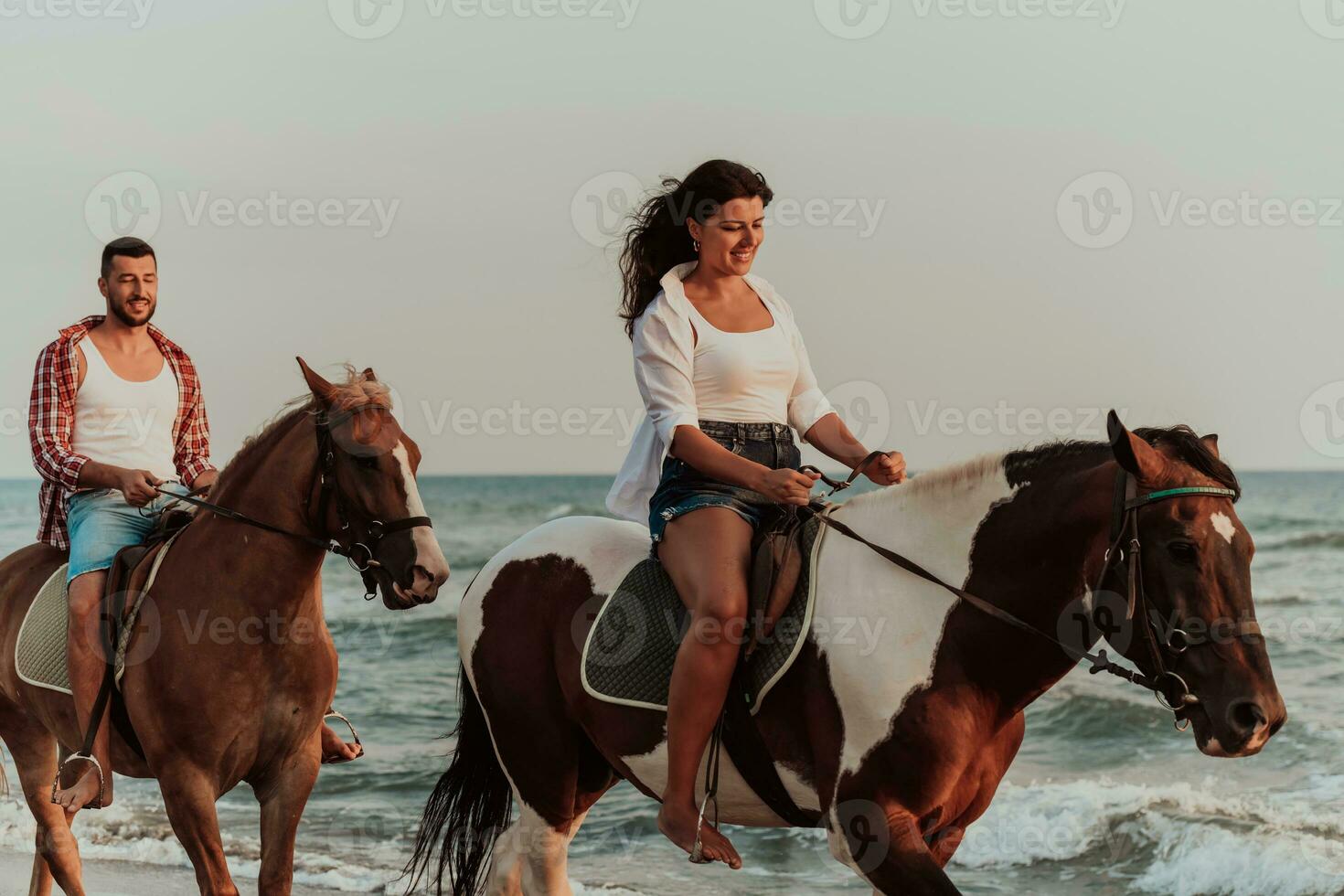 A loving couple in summer clothes riding a horse on a sandy beach at sunset. Sea and sunset in the background. Selective focus photo