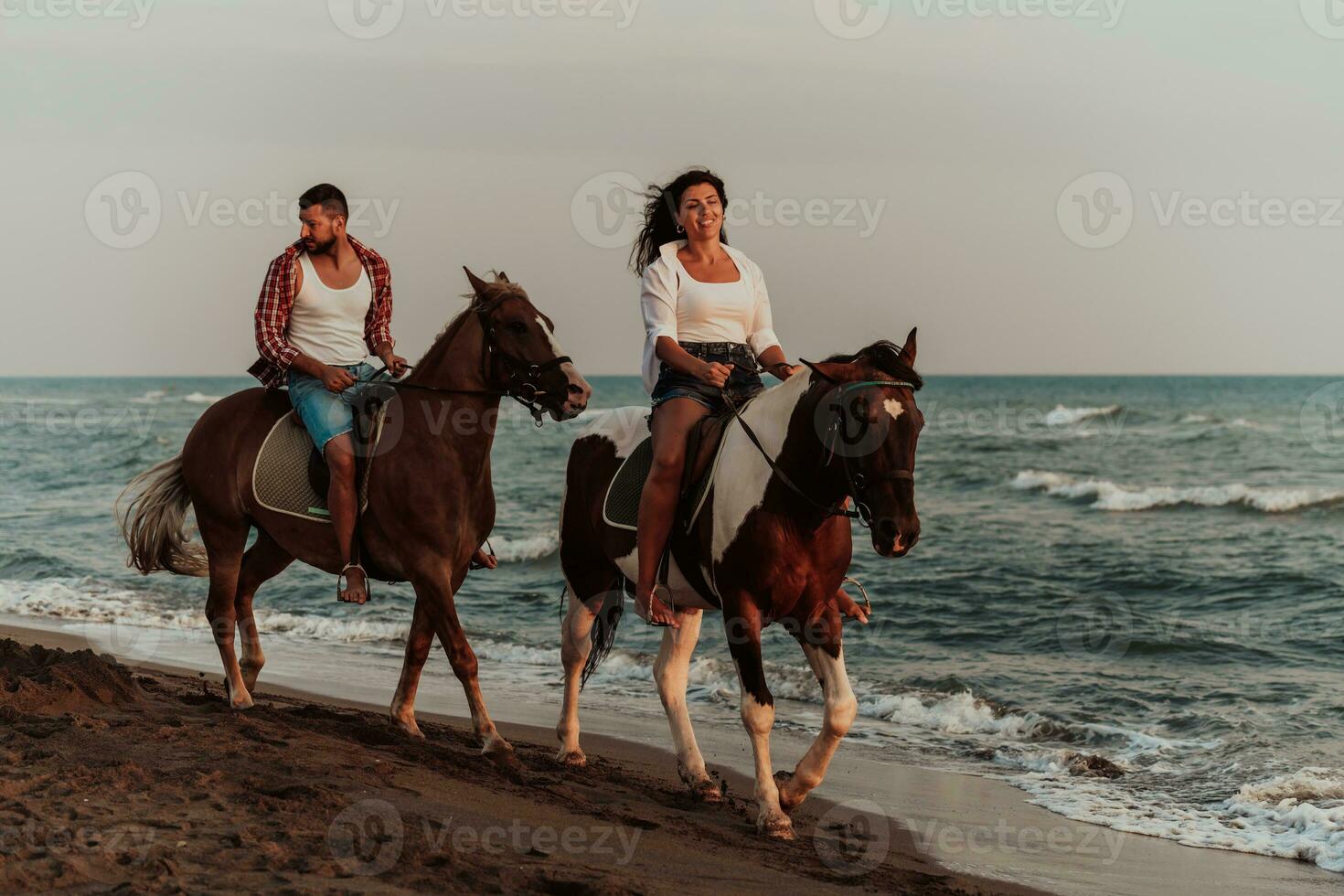 A loving couple in summer clothes riding a horse on a sandy beach at sunset. Sea and sunset in the background. Selective focus photo