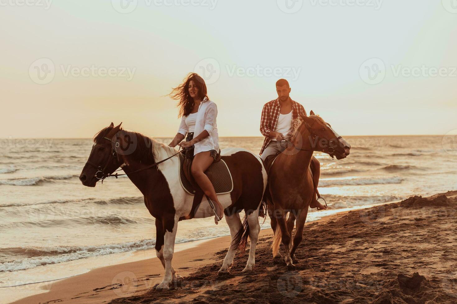 A loving couple in summer clothes riding a horse on a sandy beach at sunset. Sea and sunset in the background. Selective focus photo