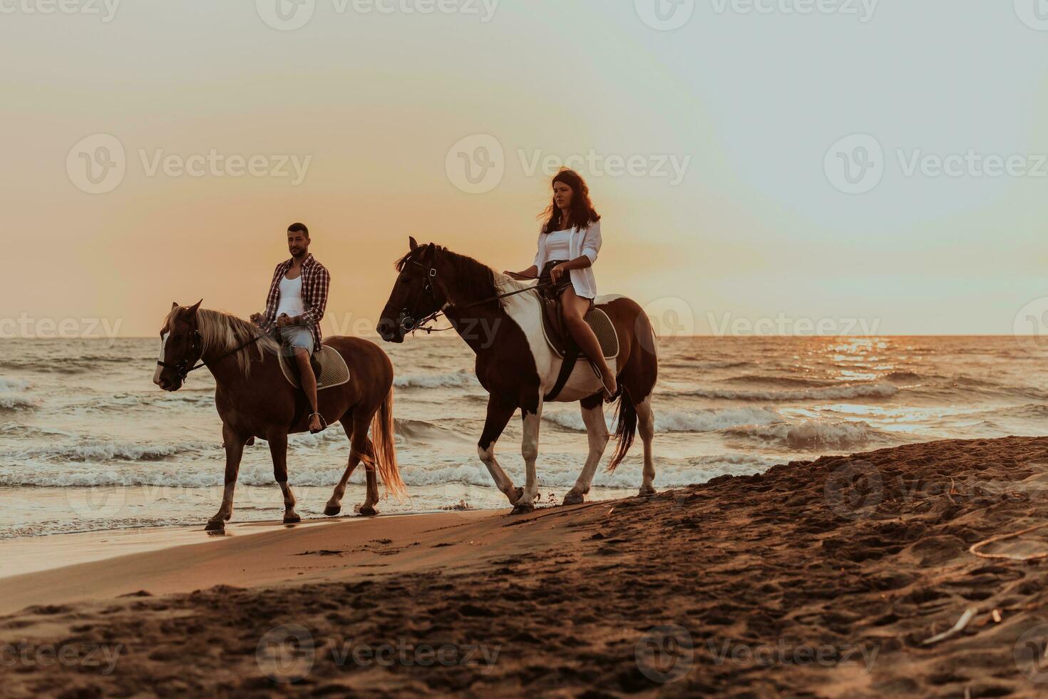 una pareja amorosa vestida de verano montando a caballo en una playa de arena al atardecer. mar y puesta de sol de fondo. enfoque selectivo foto