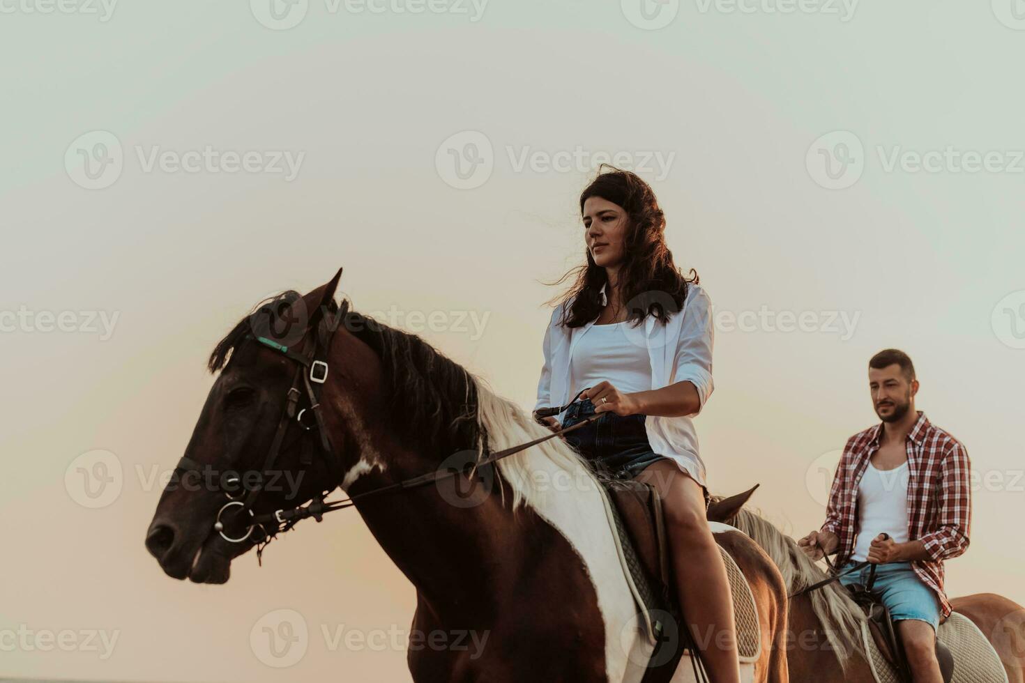 A loving couple in summer clothes riding a horse on a sandy beach at sunset. Sea and sunset in the background. Selective focus photo