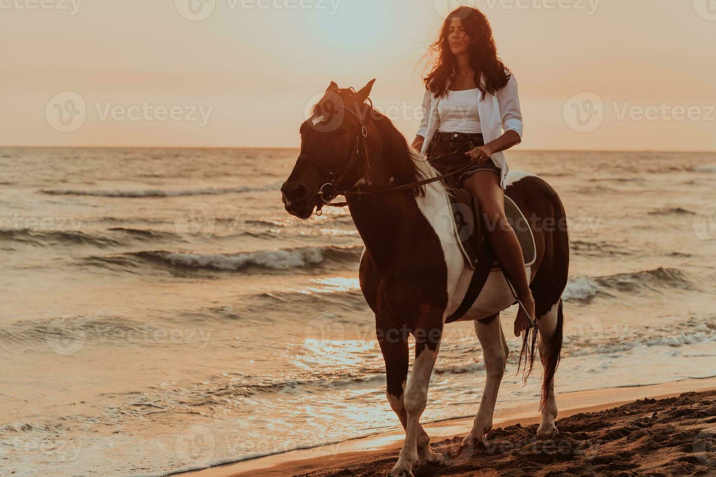 Woman in summer clothes enjoys riding a horse on a beautiful sandy beach at sunset. Selective focus photo