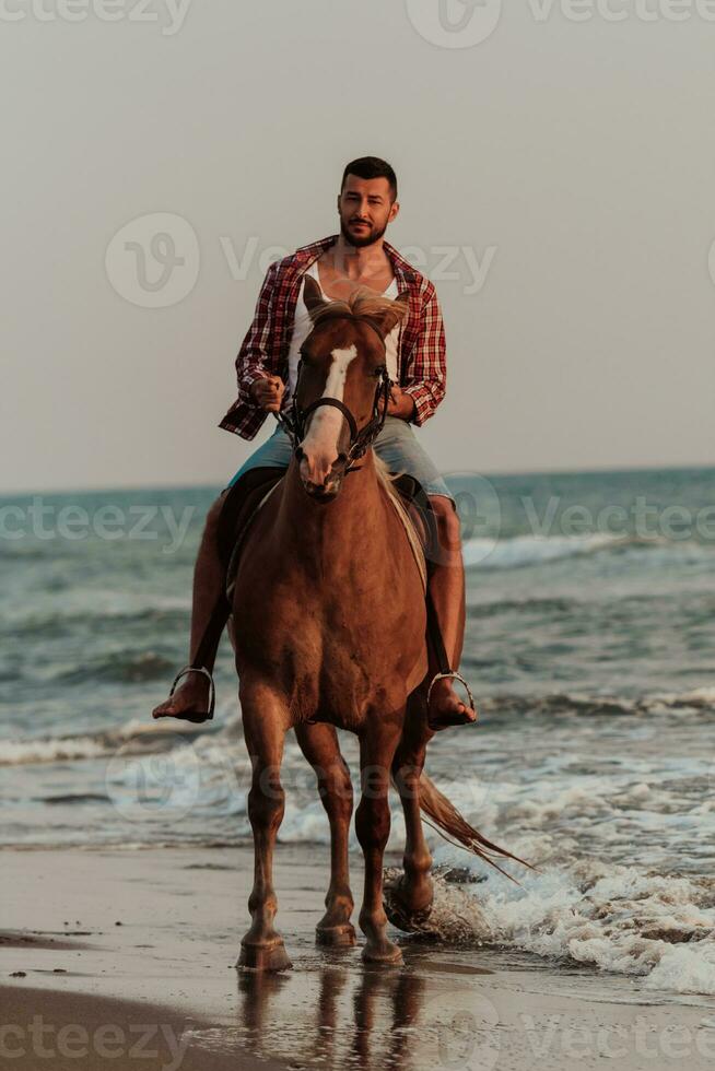 A modern man in summer clothes enjoys riding a horse on a beautiful sandy beach at sunset. Selective focus photo