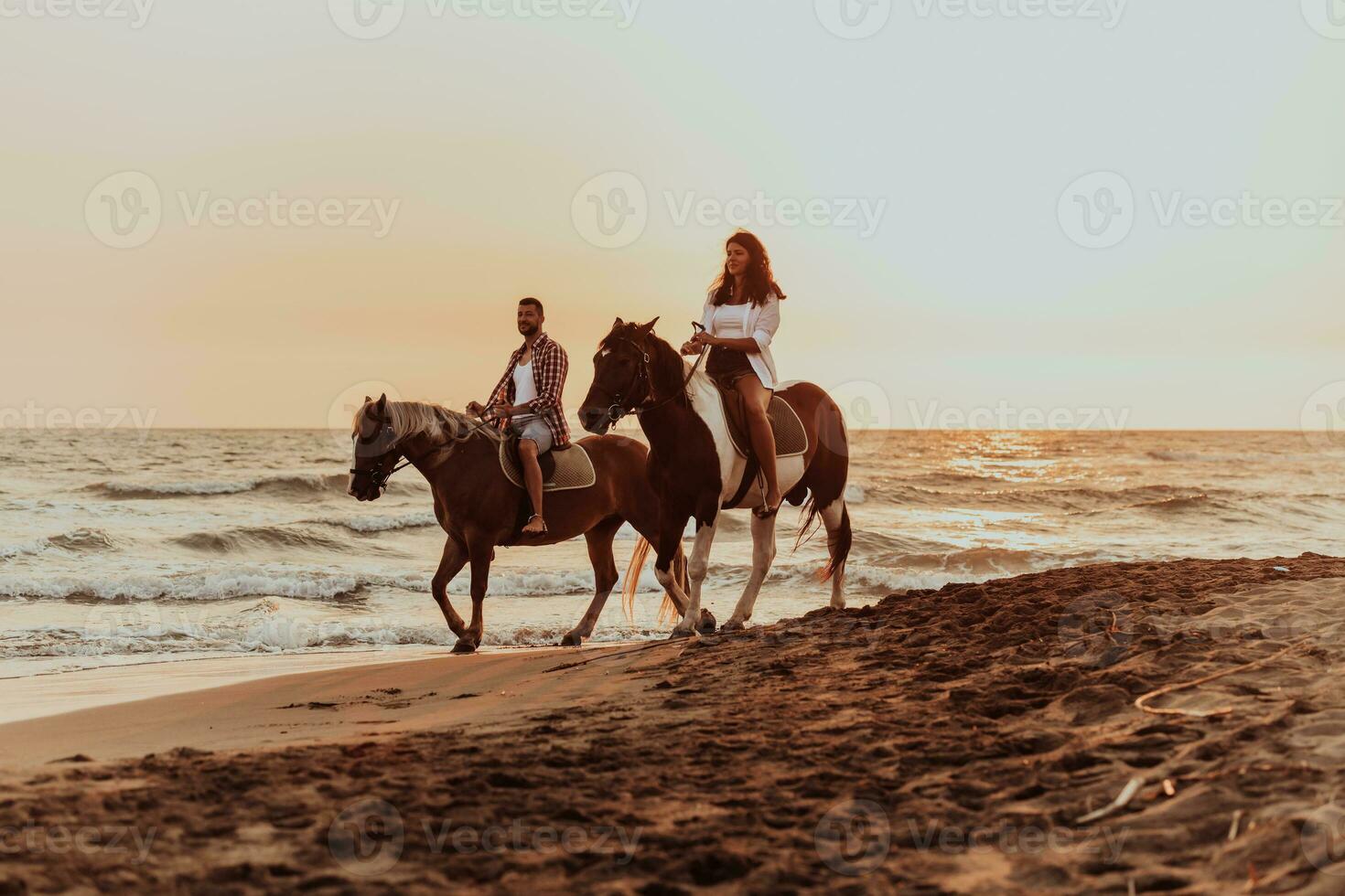 A loving couple in summer clothes riding a horse on a sandy beach at sunset. Sea and sunset in the background. Selective focus photo