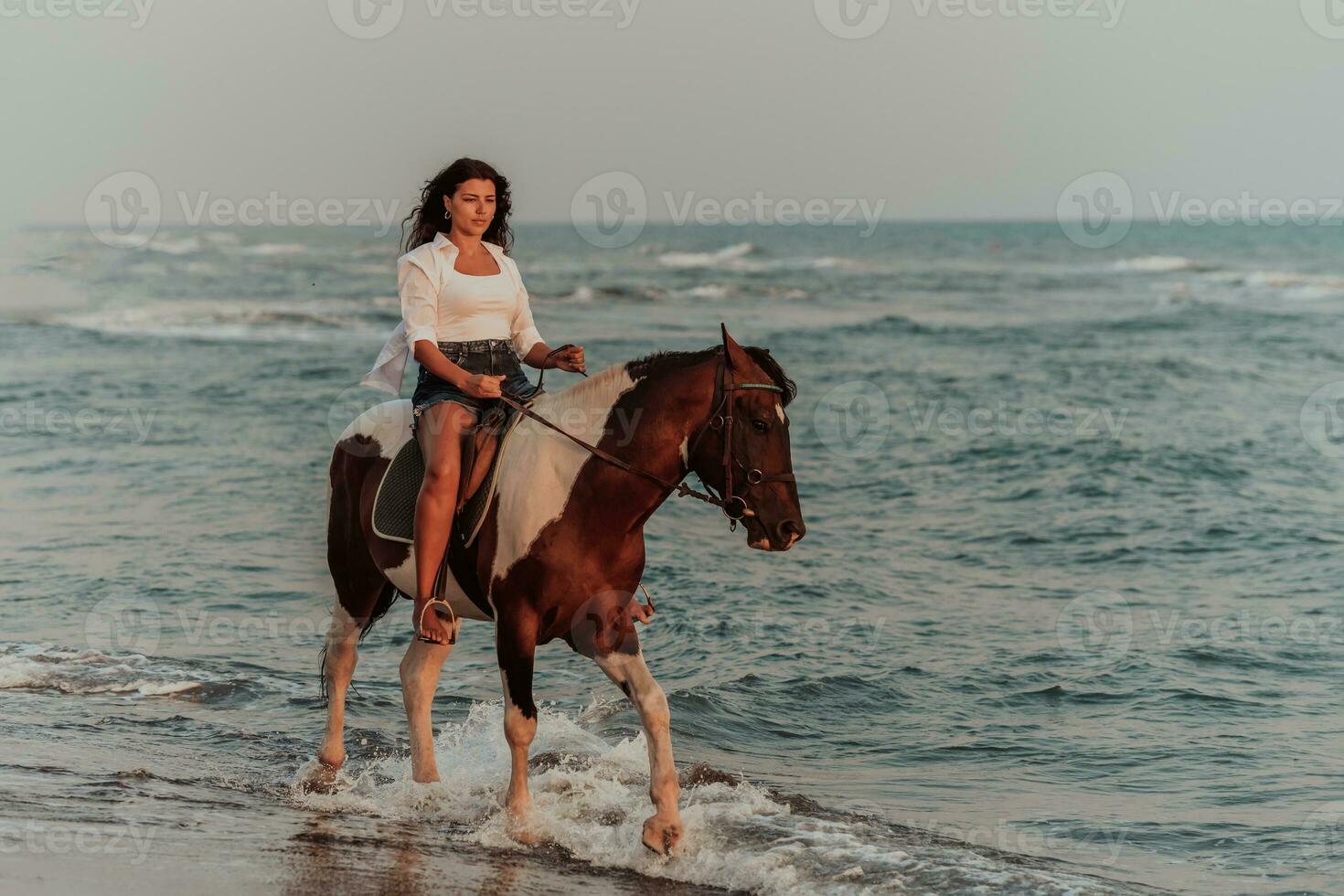 mujer vestida de verano disfruta montando a caballo en una hermosa playa de arena al atardecer. enfoque selectivo foto