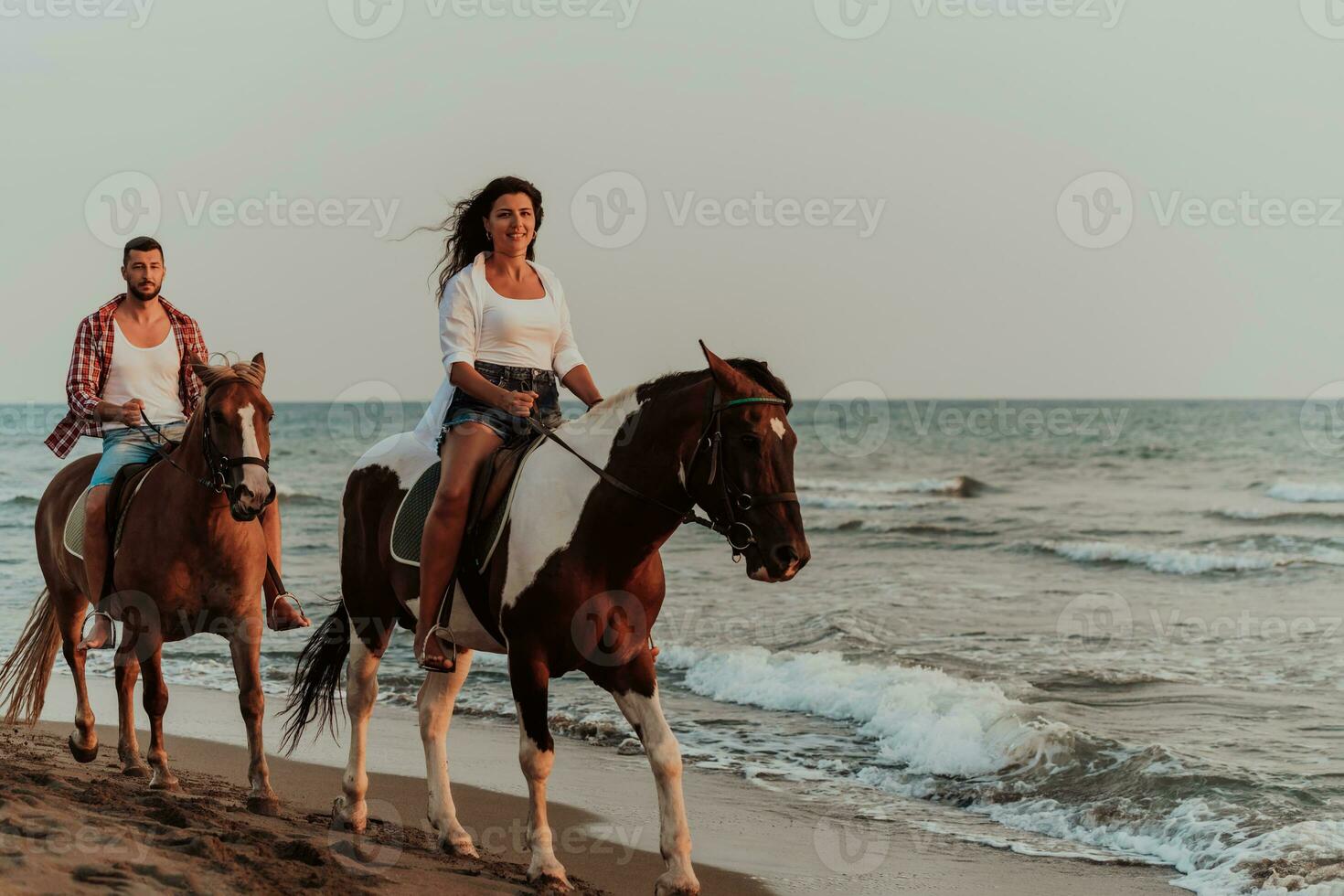 una pareja amorosa vestida de verano montando a caballo en una playa de arena al atardecer. mar y puesta de sol de fondo. enfoque selectivo foto