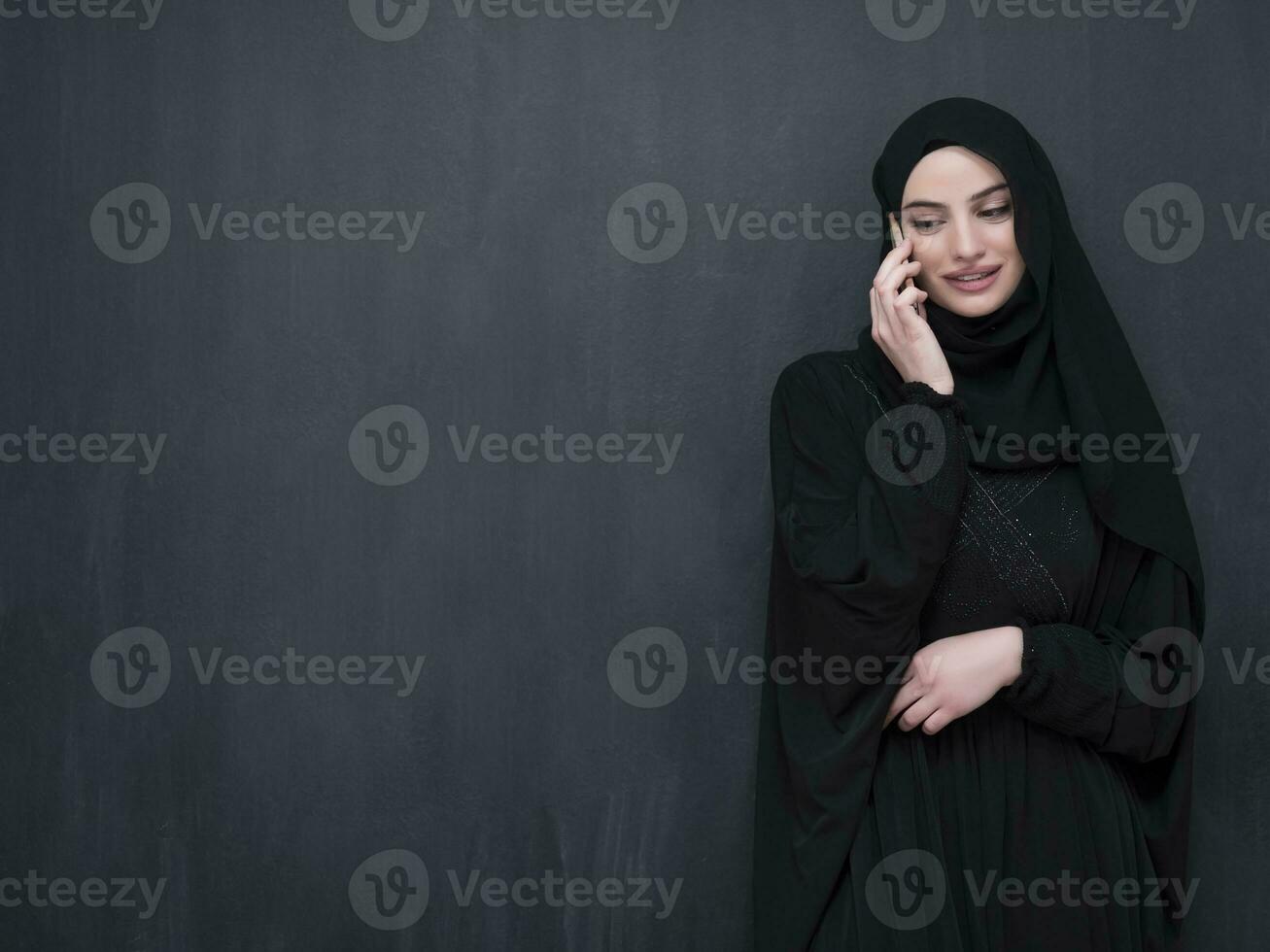 Young modern muslim business woman using smartphone wearing hijab clothes in front of black chalkboard photo