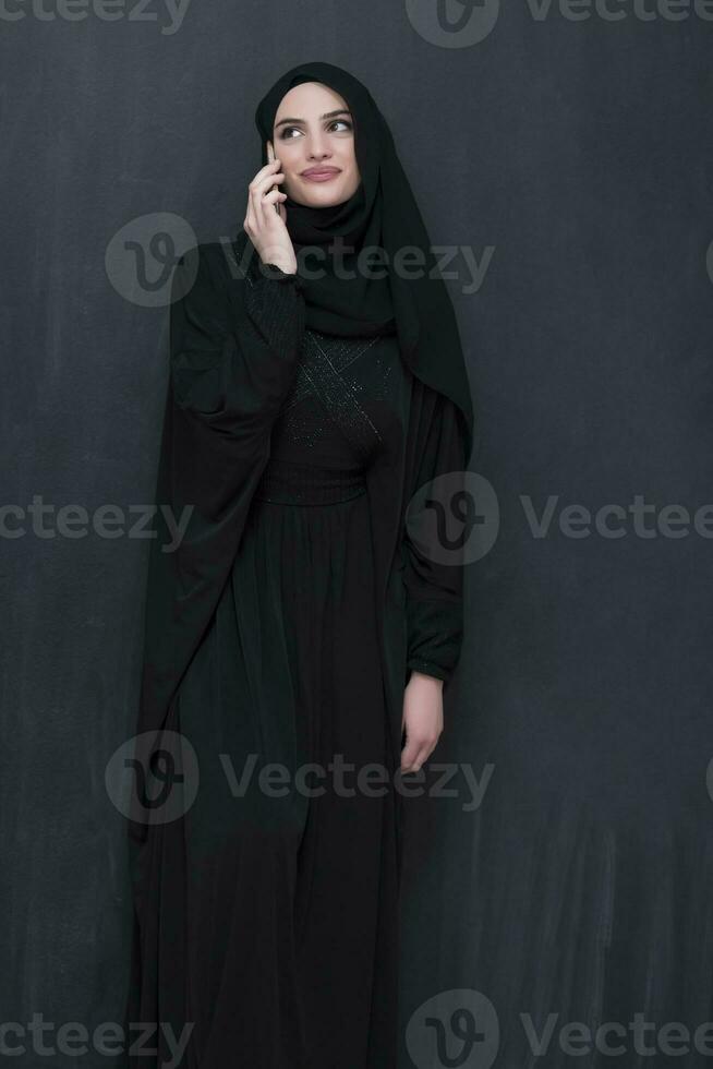 Young modern muslim business woman using smartphone wearing hijab clothes in front of black chalkboard photo