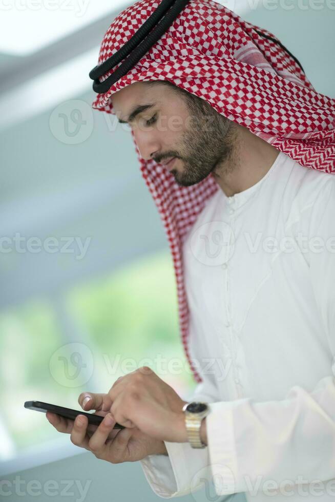 Young modern Muslim Arabian businessmen wearing traditional clothes while using smartphones at home. High-quality photo