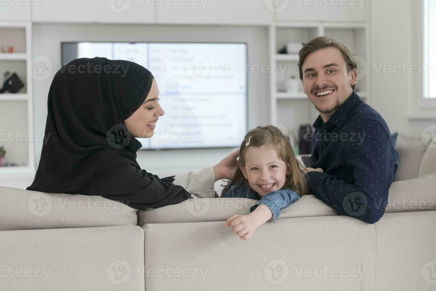 Happy Muslim family with daughter woman in traditional fashionable dress having fun and good time together while sitting on sofa photo