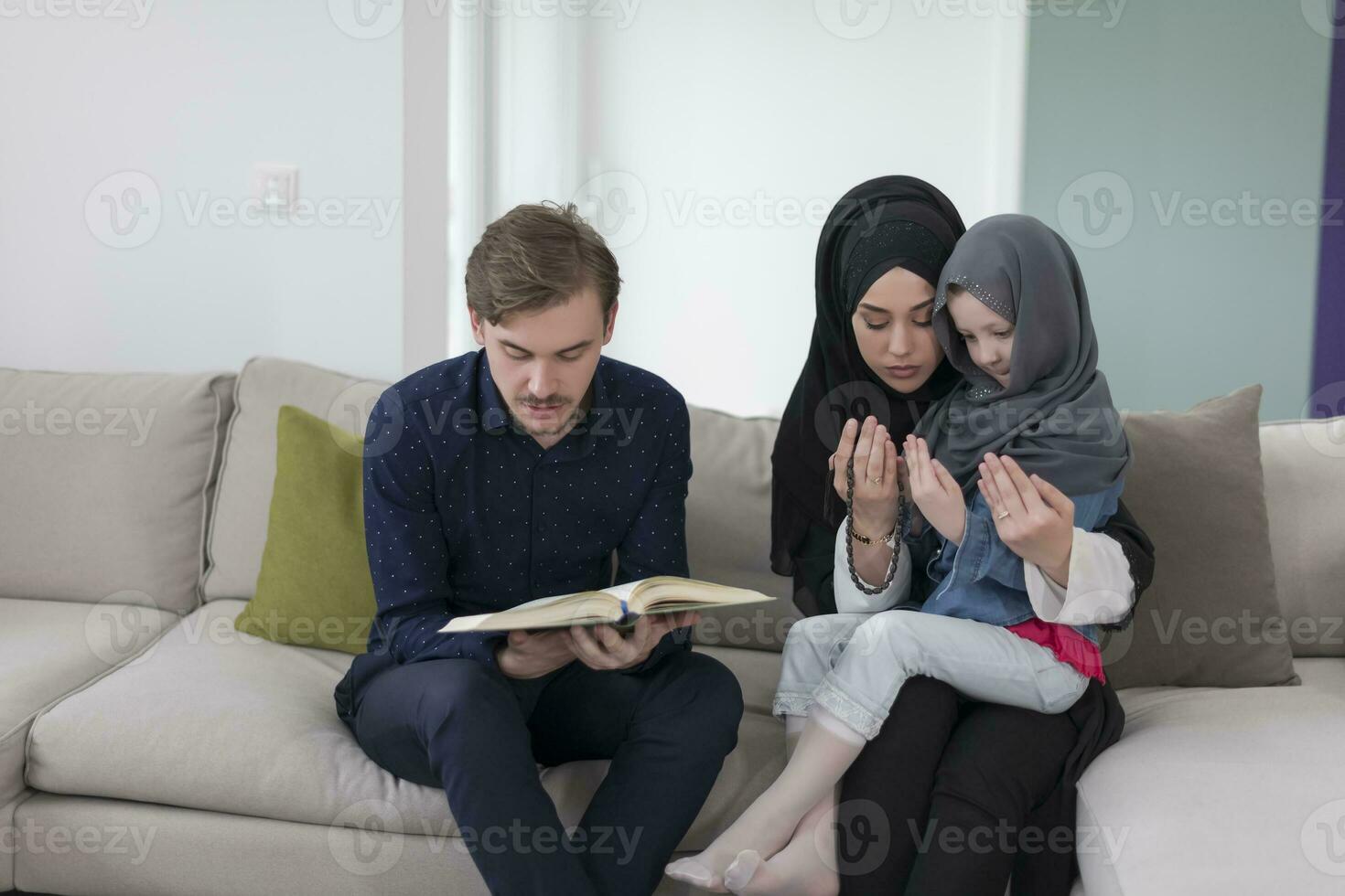 Traditional muslim family parents with children reading Quran and praying together on the sofa before iftar dinner during a ramadan feast at home photo