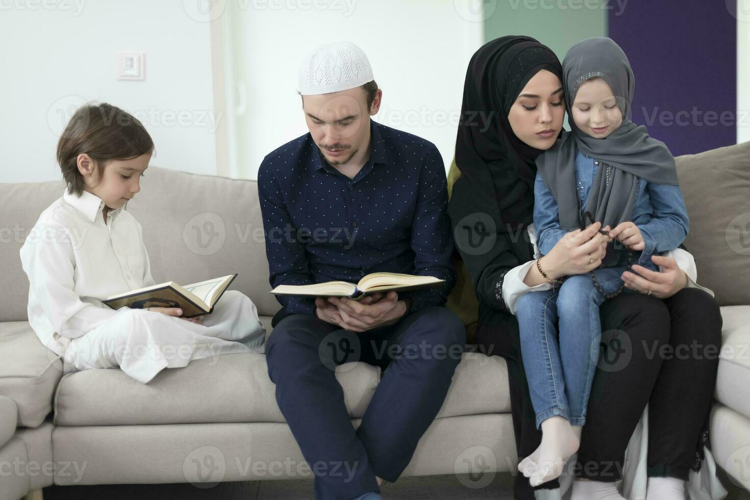 Traditional muslim family parents with children reading Quran and praying together on the sofa before iftar dinner during a ramadan feast at home photo