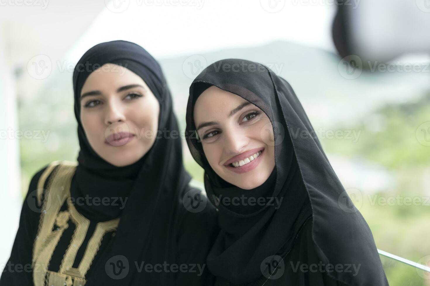 young beautiful muslim women in fashionable dress with hijab using mobile phone while taking selfie picture on the balcony representing modern islam fashion technology and ramadan kareem concept photo
