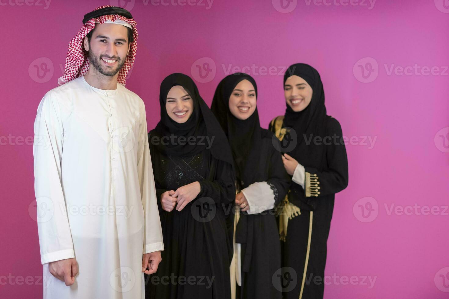 Group portrait of young Muslim people Arabian men with three Muslim women in a fashionable dress with hijab isolated on a pink background photo