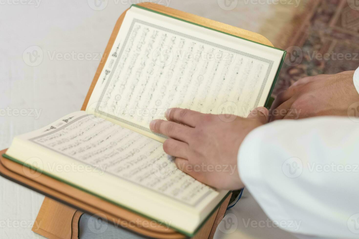 young arabian muslim man in traditional clothes reading holy book Quran on the praying carpet before iftar dinner during a ramadan feast at home photo