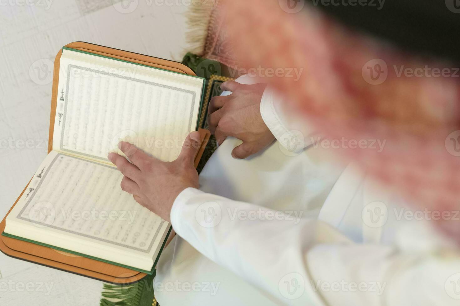 young arabian muslim man in traditional clothes reading holy book Quran on the praying carpet before iftar dinner during a ramadan feast at home photo