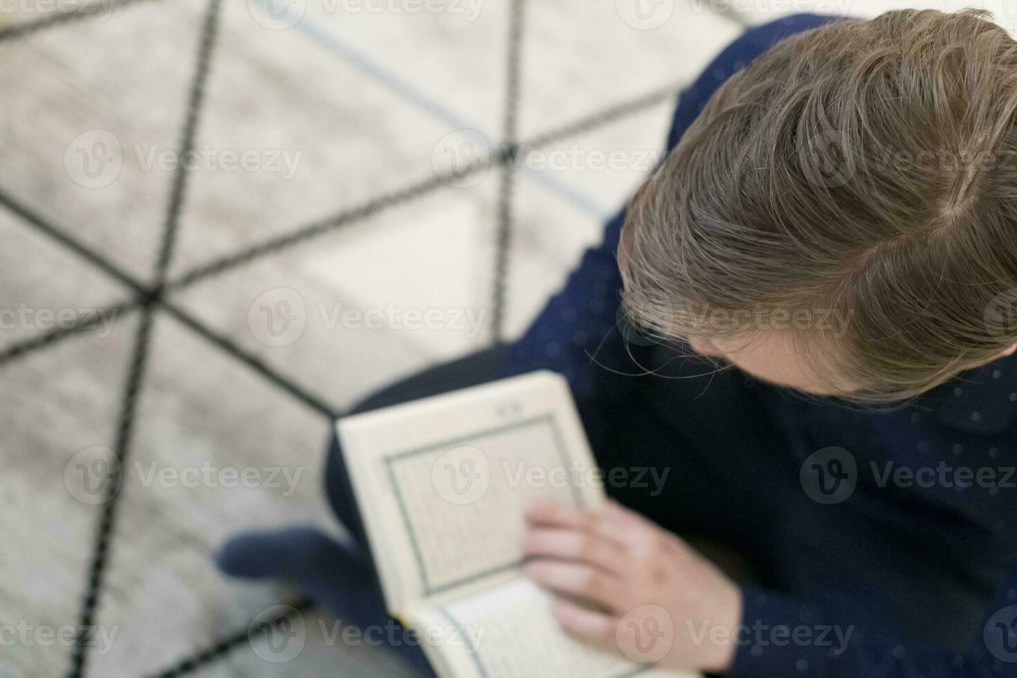 Young muslim man sitting on the floor while reading holy book Quran before iftar dinner during a ramadan feast at home photo