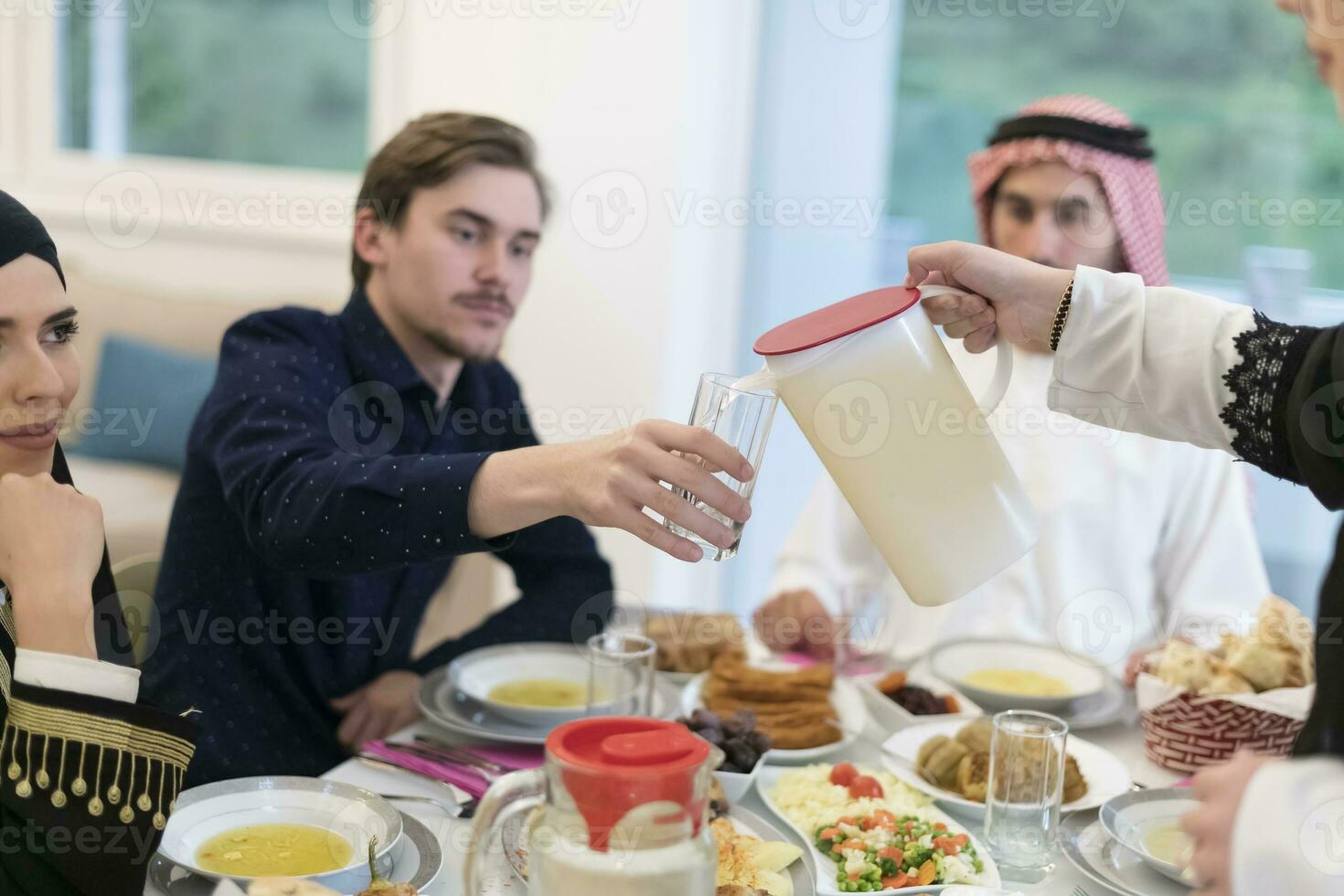 eid Mubarak musulmán familia teniendo iftar cena Bebiendo agua a descanso banquete. comiendo tradicional comida durante Ramadán banquete mes a hogar. el islámico halal comiendo y Bebiendo a moderno occidental isla foto