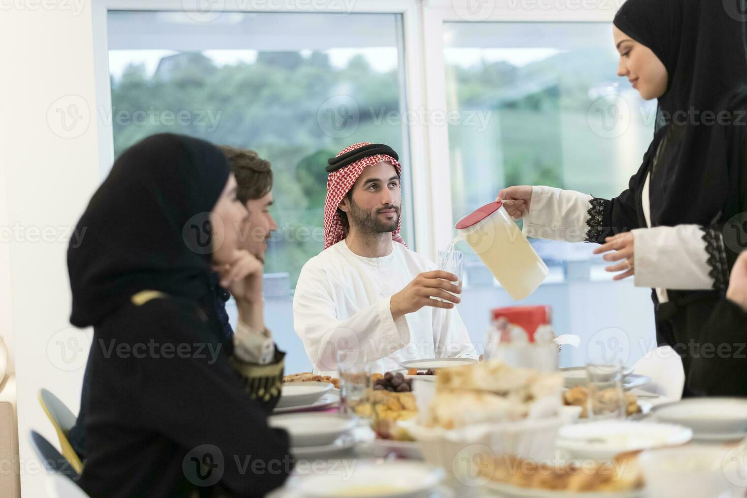 Eid Mubarak Muslim family having Iftar dinner drinking water to break feast. Eating traditional food during Ramadan feasting month at home. The Islamic Halal Eating and Drinking at modern western Isla photo