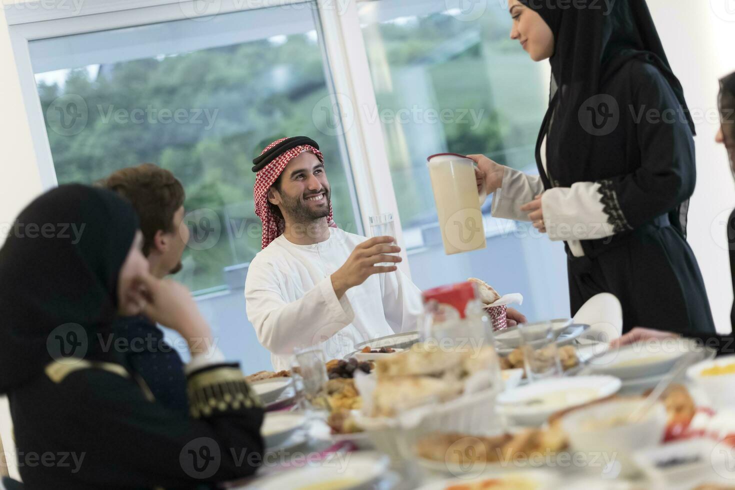 eid Mubarak musulmán familia teniendo iftar cena Bebiendo agua a descanso banquete. comiendo tradicional comida durante Ramadán banquete mes a hogar. el islámico halal comiendo y Bebiendo a moderno occidental isla foto