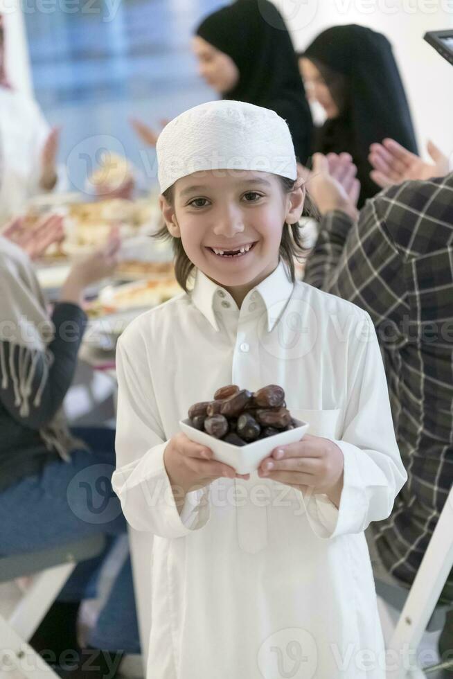 Eid Mubarak Muslim family having Iftar dinner little boy holding a plate full of sweet dates to break feast. Eating traditional food during Ramadan feasting month at home. The Islamic Halal Eating photo